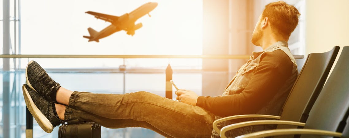 Foto homem sentado na cadeira do aeroporto com os pés na bagagem olhando para o avião