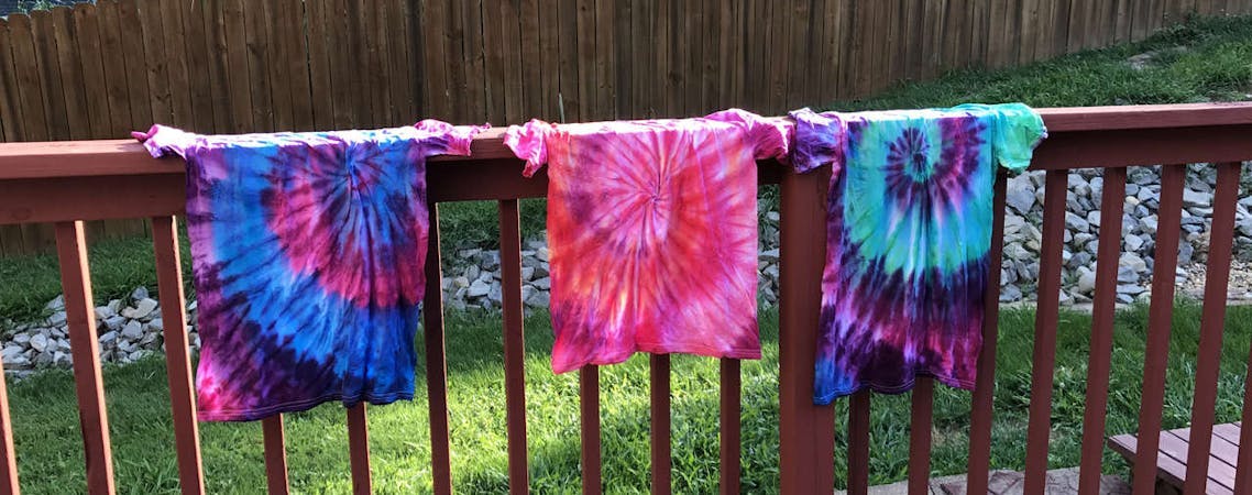 Camisetas Tie Dye penduradas em uma cerca de madeira
