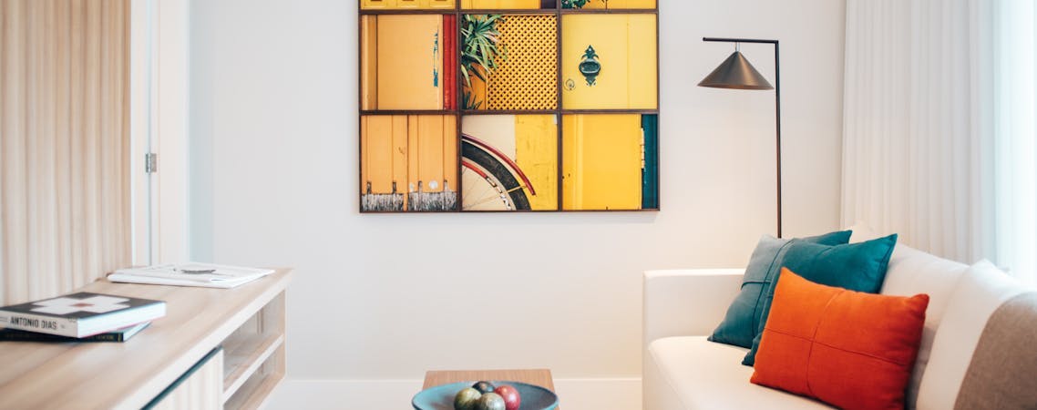 Foto de sala com sofá branco com almofada coloridas e quadro na parede.