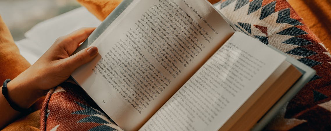 Foto pessoa lendo livro sobre tecido marrom e bege.